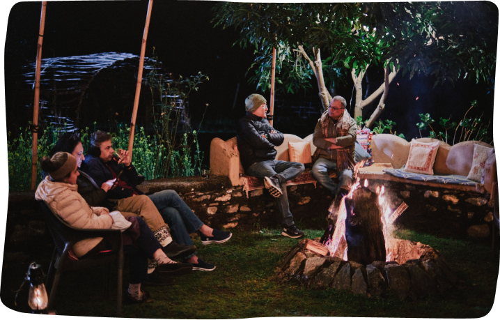 Guests gathered around an evening bonfire under the trees